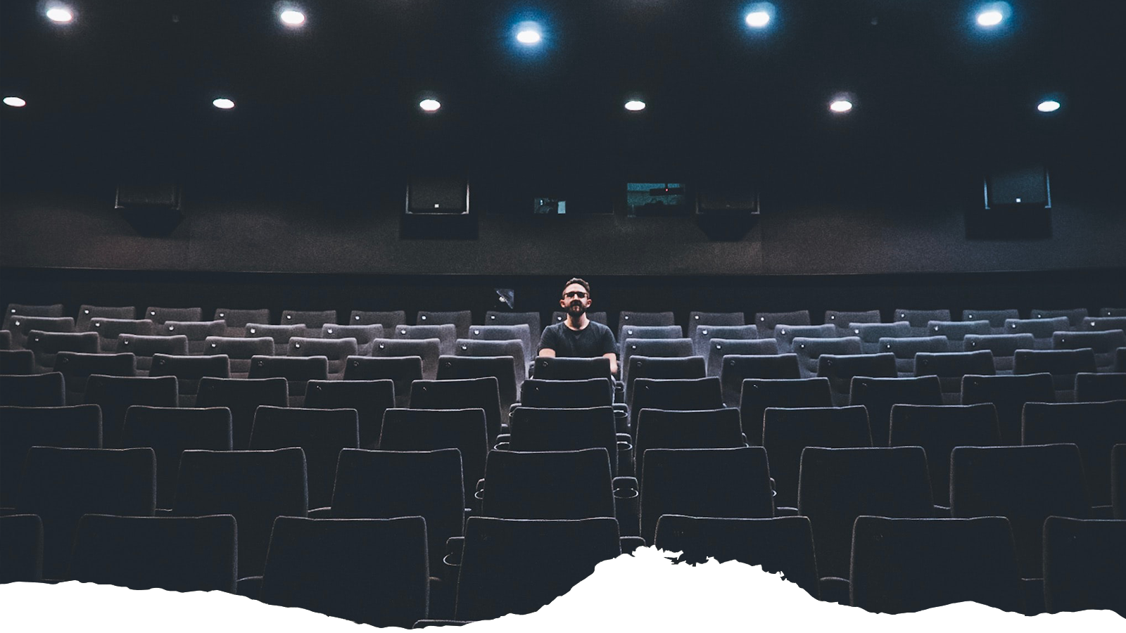 A man sits in an empty theater, illustrative of event closures from the COVID-19 pandemic.