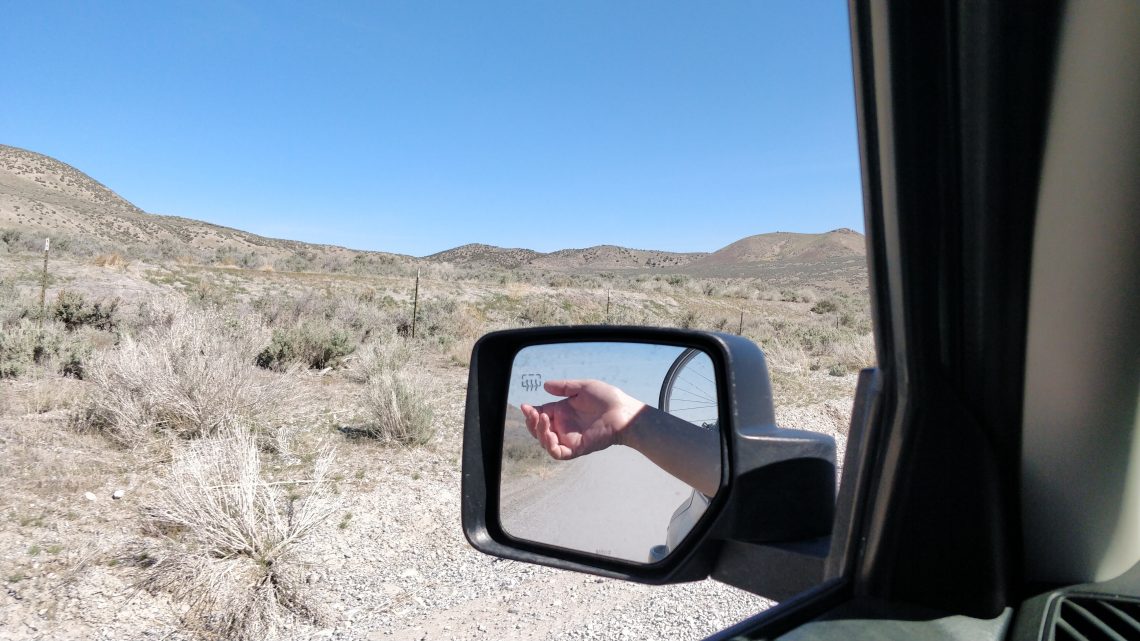 A white woman's hand is shown in the side mirror with a desert landscape behind.