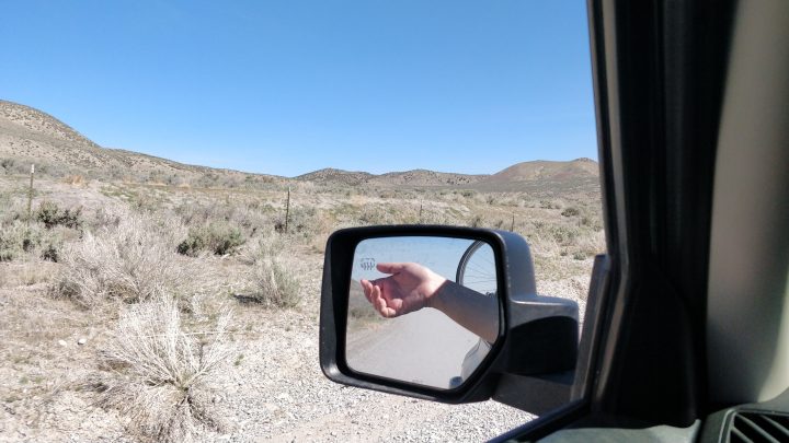 A white woman's hand is shown in the side mirror with a desert landscape behind.