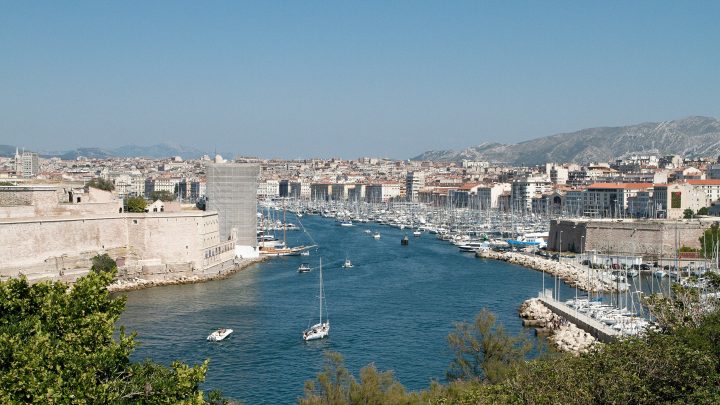 port of marseilles is shown with water in foreground and boats, buildings around harbor