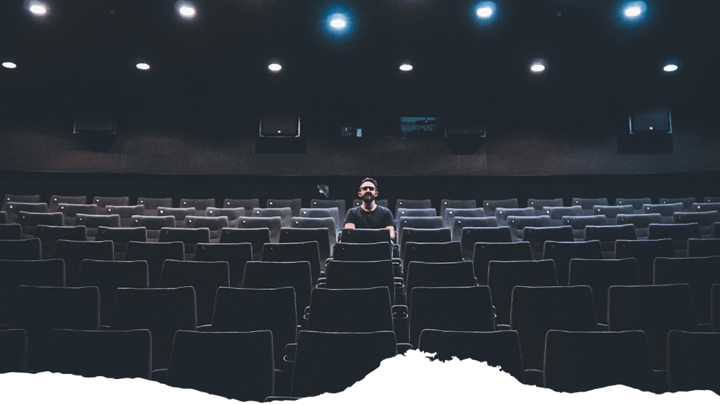 A man sits in an empty theater, illustrative of event closures from the COVID-19 pandemic.